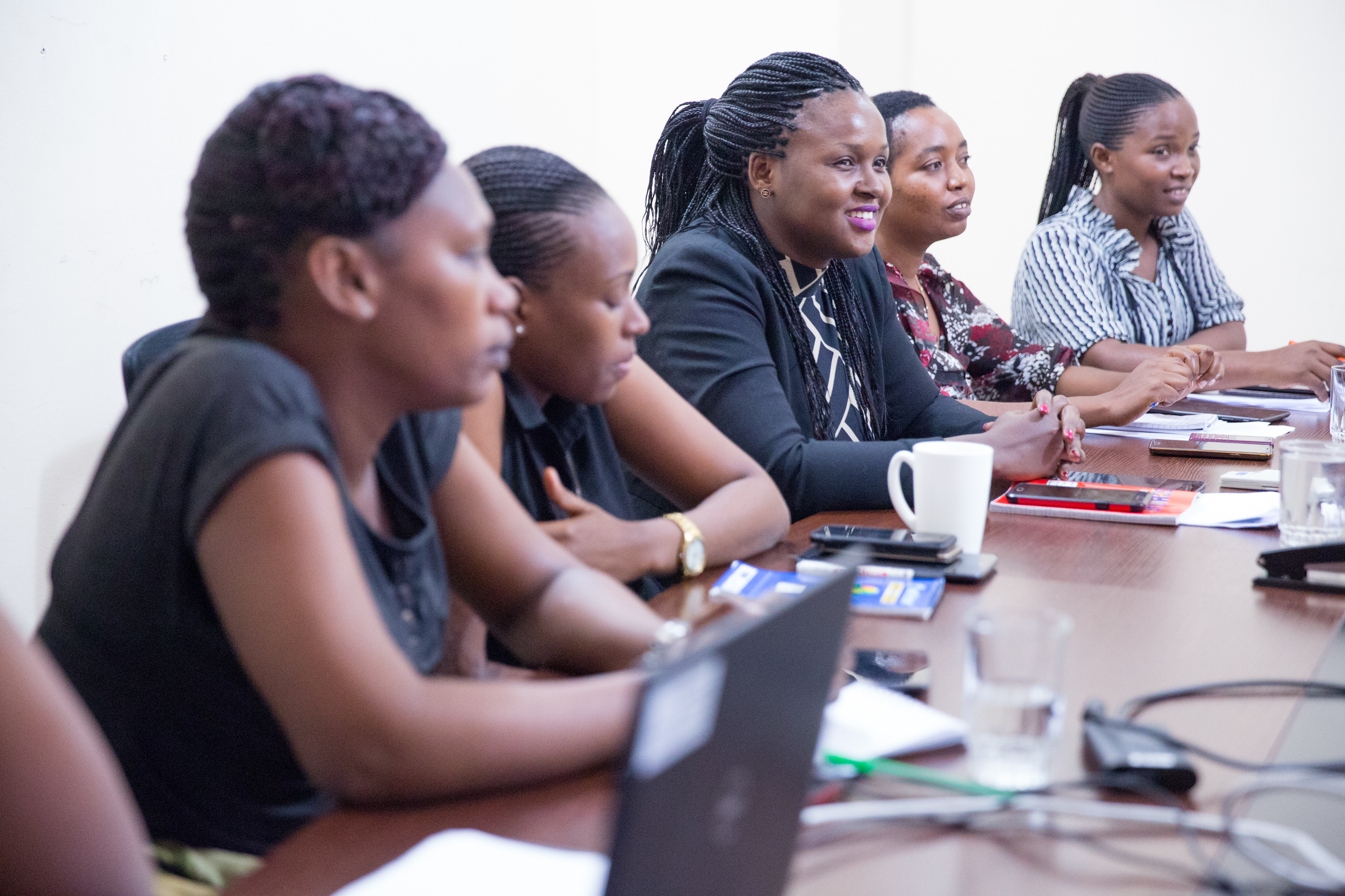 Ritha Mboneko participates in a meeting with her Tanzanian and UCSF colleagues. She is shown smiling and listening at a conference table.