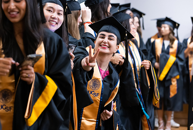 Masters' student flashing a peace sign amongst a crowd of other students graduating with her