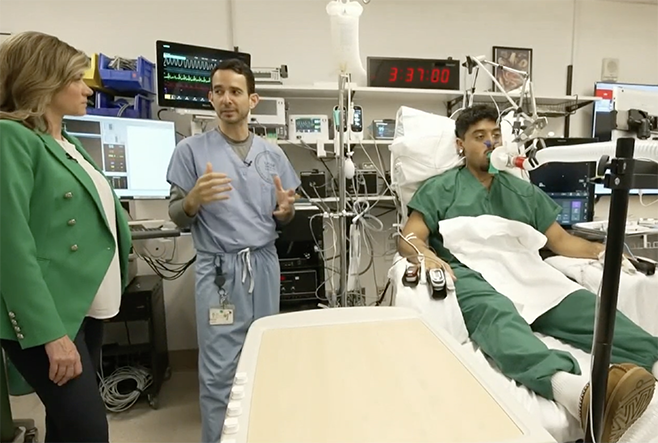 A doctor having a conversation with a reporter in a hospital room with a patient in a bed.